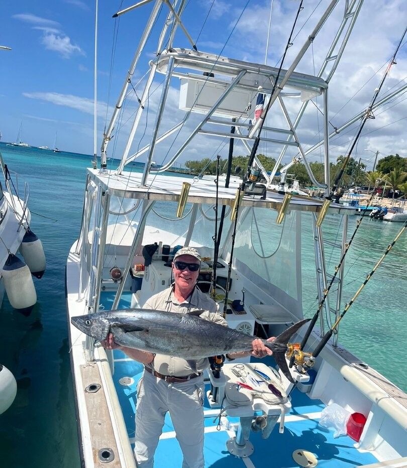 Angler holding caught King Mackerel on fishing boat deck in tropical waters