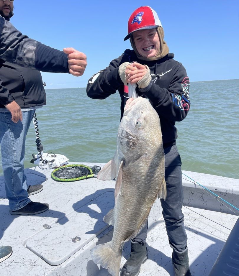 Large black drum fish being held on fishing boat deck over water