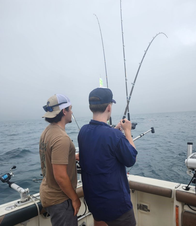 Two anglers fishing from boat deck with multiple fishing rods on foggy ocean waters