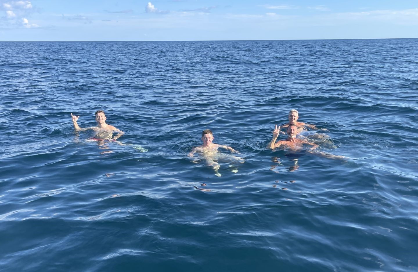 Four people swimming in deep blue ocean water under clear sky