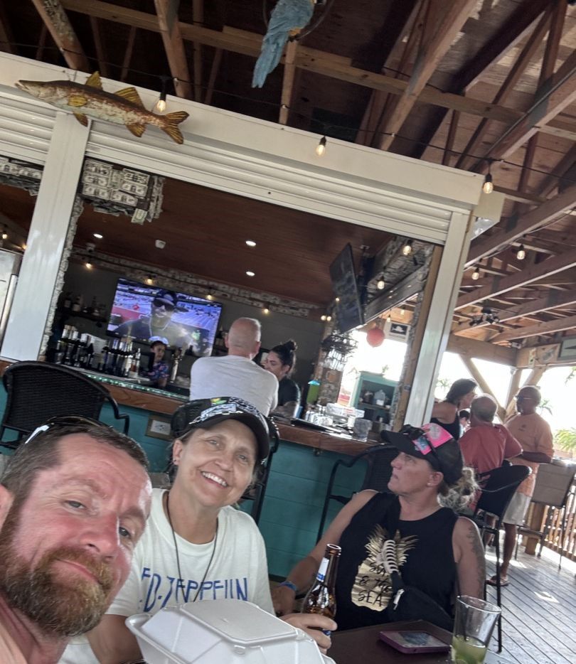 Outdoor restaurant bar area with wooden beams, decorative fish displays, and tropical parrot