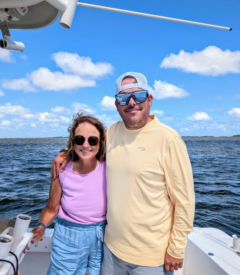 Two people posing together on a boat deck with ocean water and blue sky in background