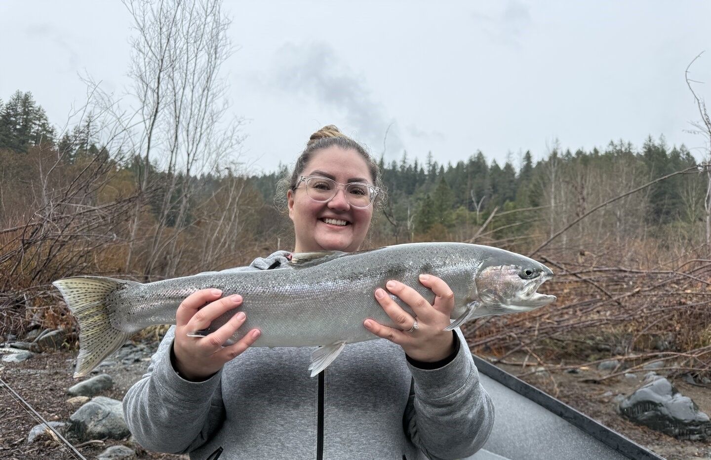 Angler holding freshly caught rainbow trout outdoors near forested riverbank
