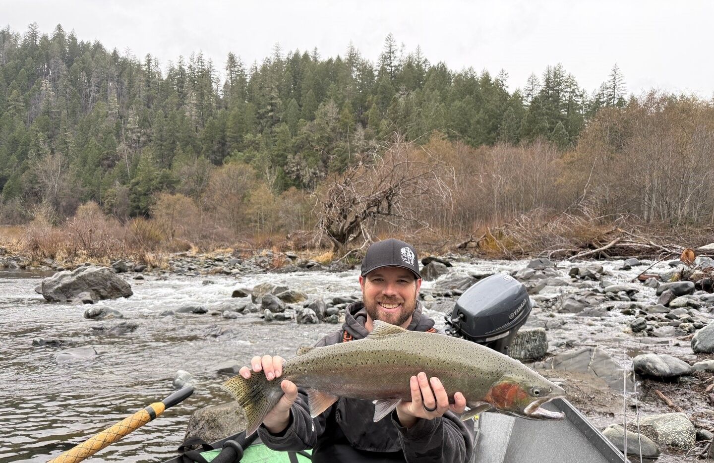Rainbow trout catch displayed outdoors near rocky river with forested hillside