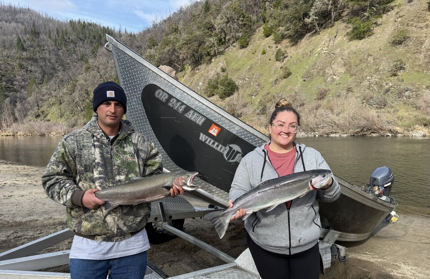 Two anglers displaying freshly caught rainbow trout beside fishing boat at lake