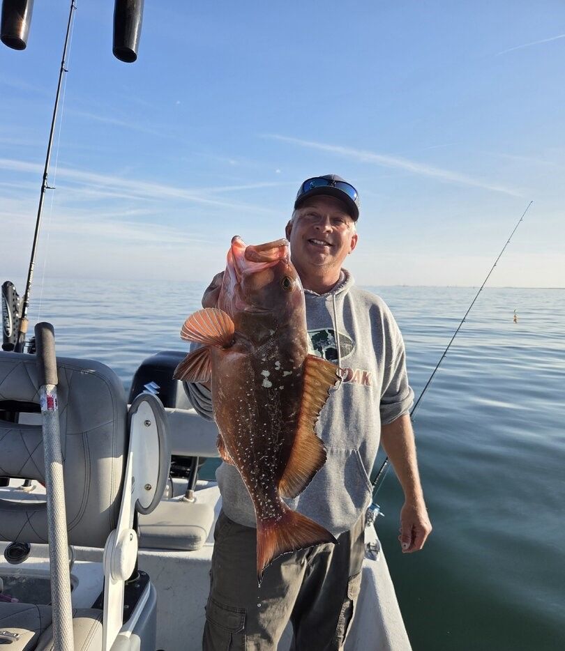 Angler holding large red grouper fish on fishing boat in calm ocean waters