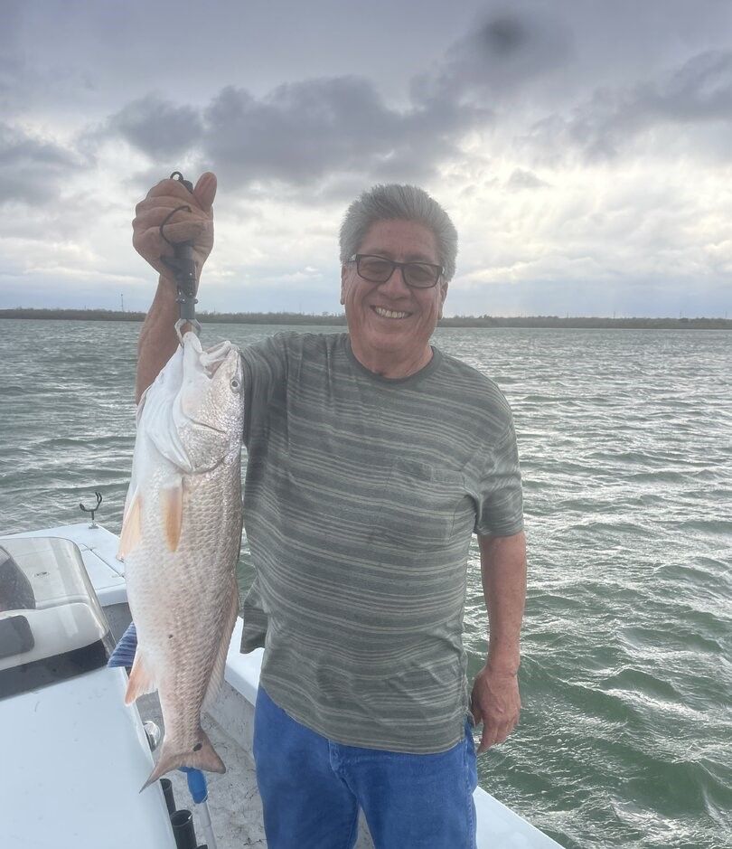 Angler holding caught redfish on boat deck with water and cloudy sky in background