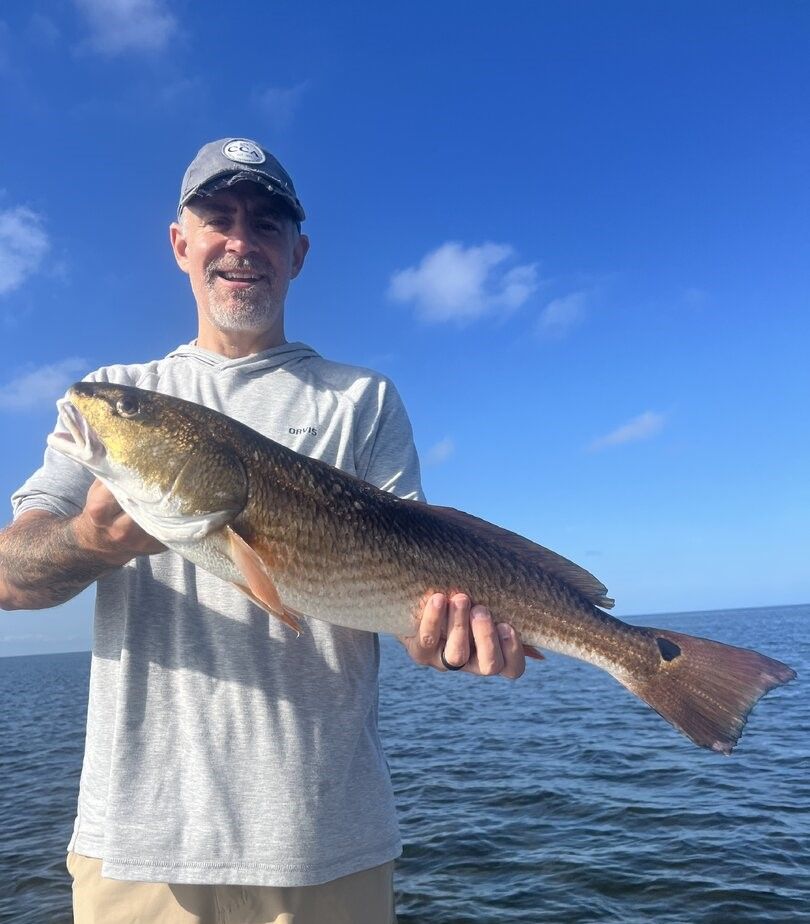 Angler holding freshly caught redfish on boat with ocean and blue sky background
