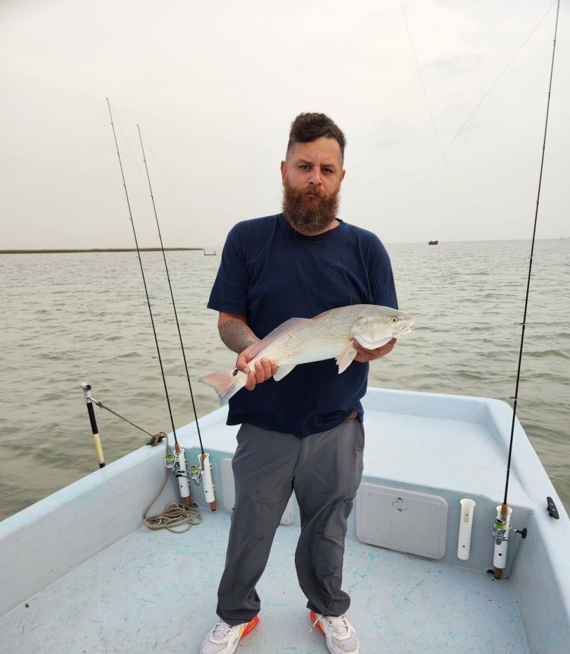 Angler holding caught redfish on fishing boat with rods visible