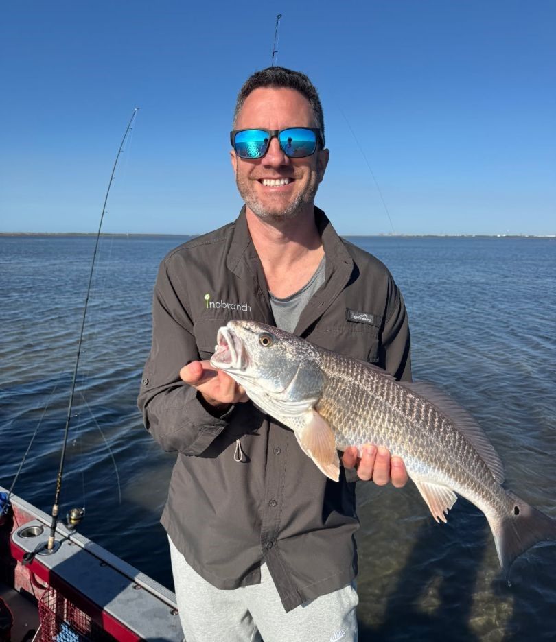 Angler holding caught redfish on fishing boat with clear blue water and sky