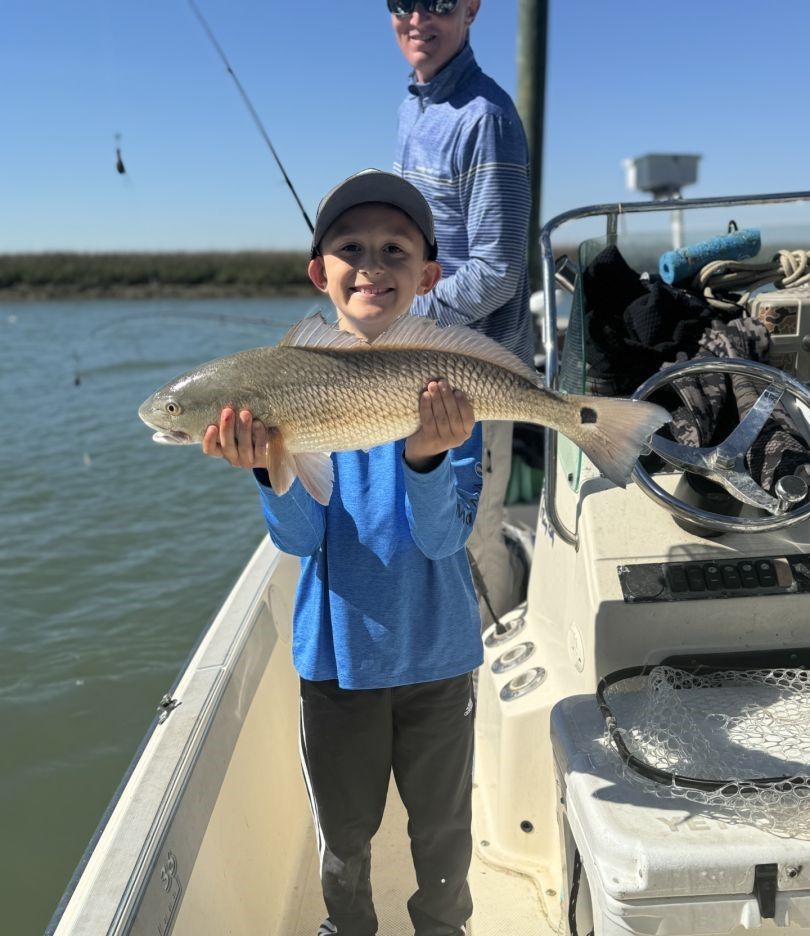 Young angler holding caught redfish on fishing boat