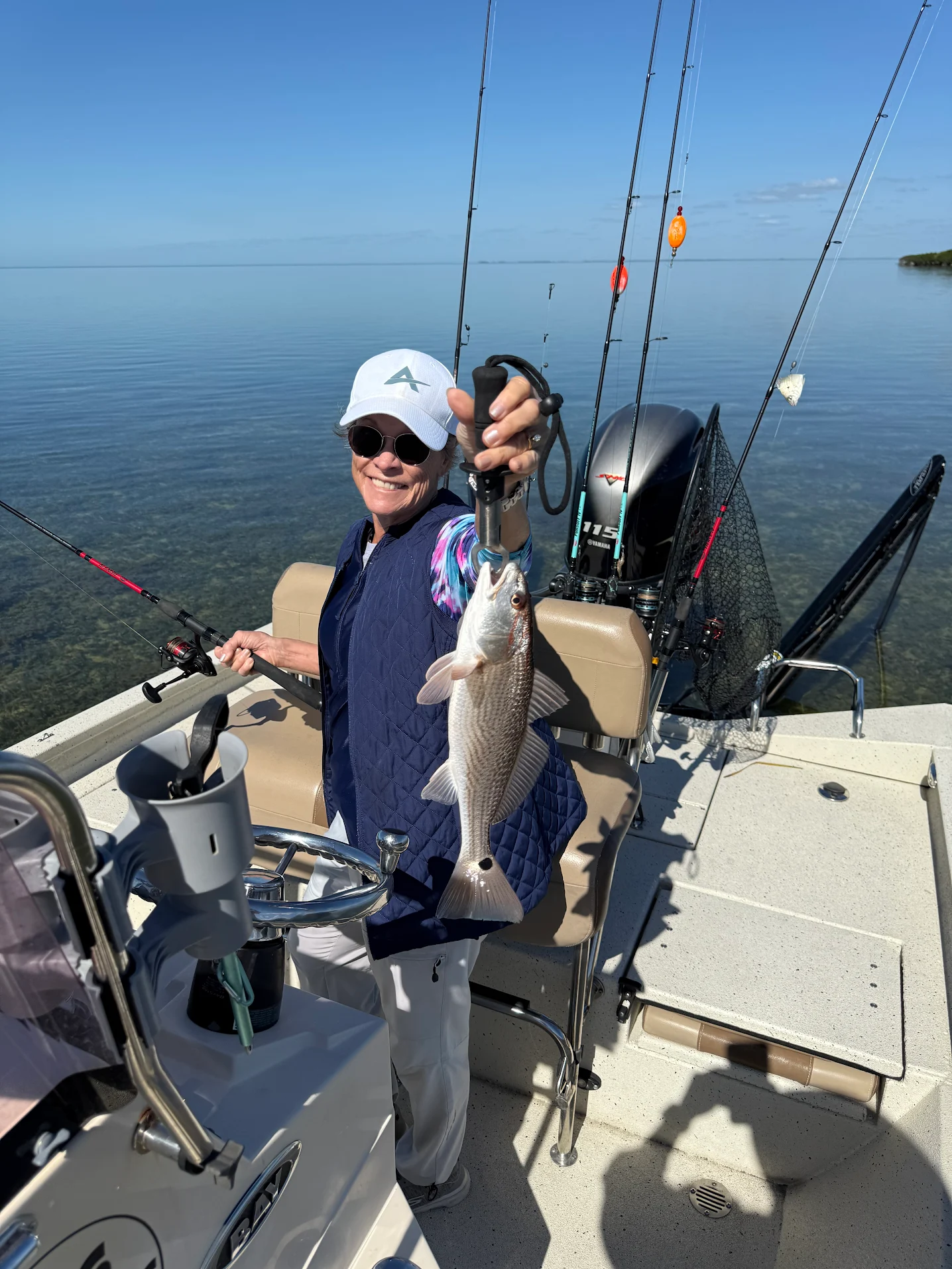 Angler holding caught redfish on fishing boat with multiple rods and calm water background