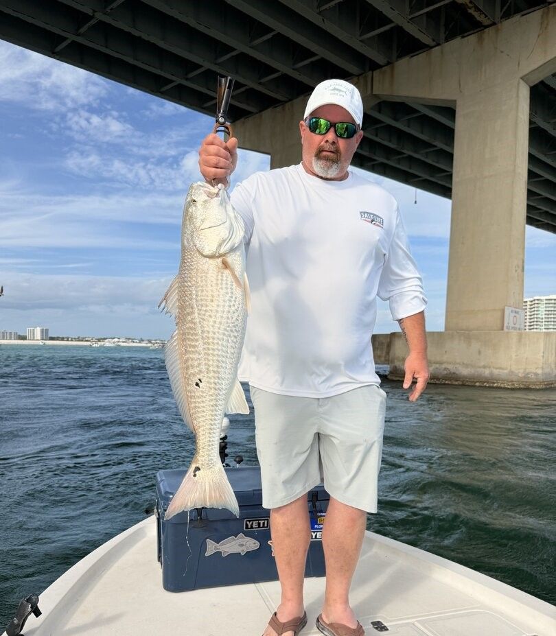 Angler holding caught redfish on fishing boat under bridge