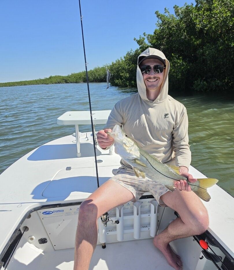 Angler holding caught snook on fishing boat in shallow water near mangroves