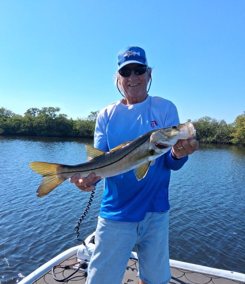 Angler holding freshly caught snook on fishing boat with water and trees in background