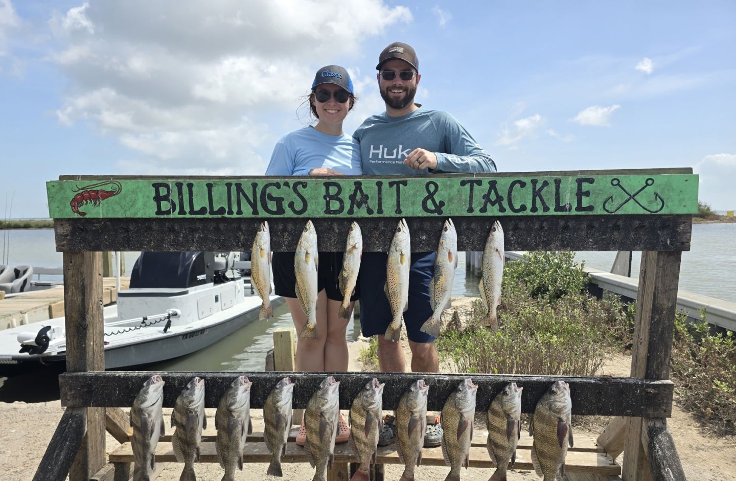 Fishing display showing 16 caught fish including speckled trout and black drum hanging from wooden cleaning station at marina