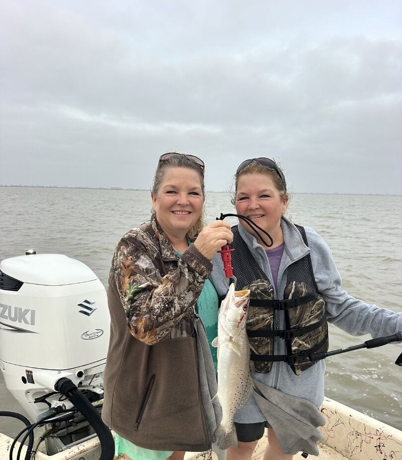 Two anglers on boat holding freshly caught speckled trout with Suzuki outboard motor visible