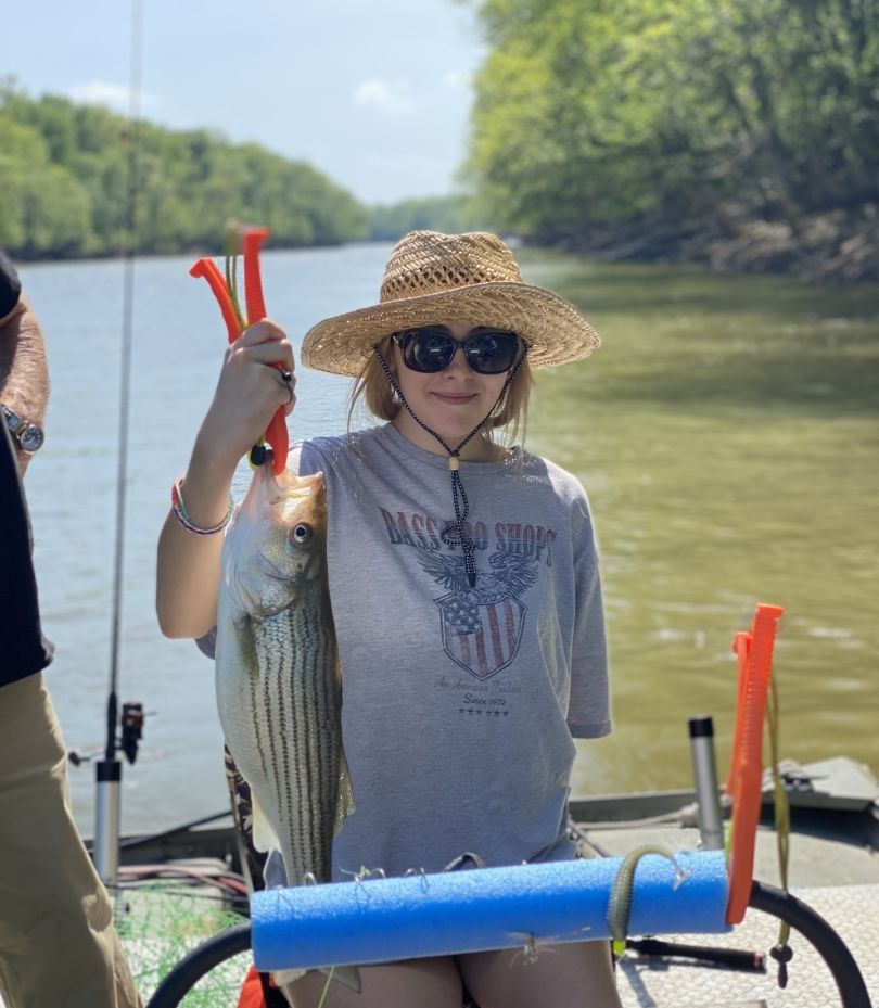 Freshly caught striped bass being displayed on fishing boat with river and trees in background