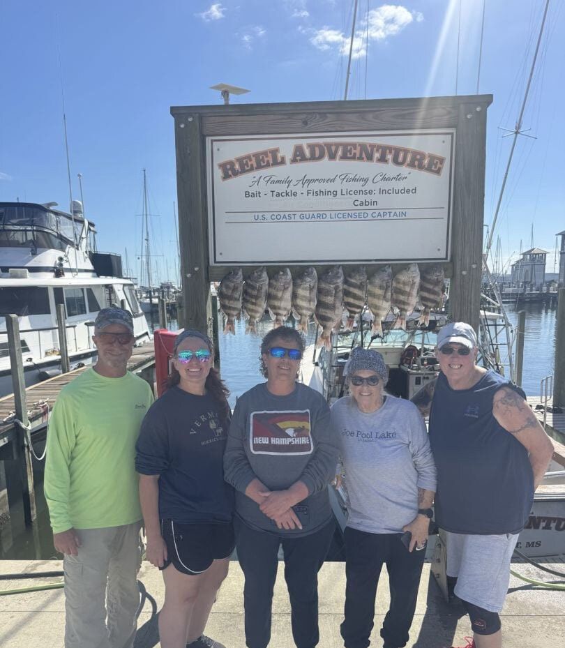 Group poses at marina dock with fishing charter sign and hanging fish display