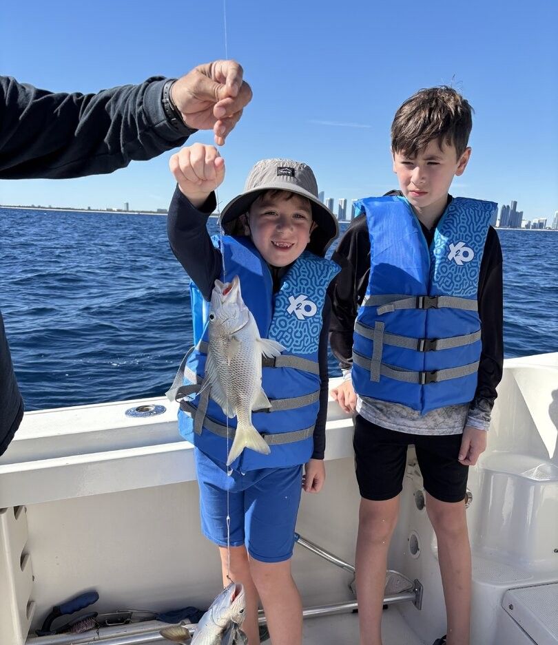 Fresh caught fish being held up on fishing boat with ocean and city skyline in background