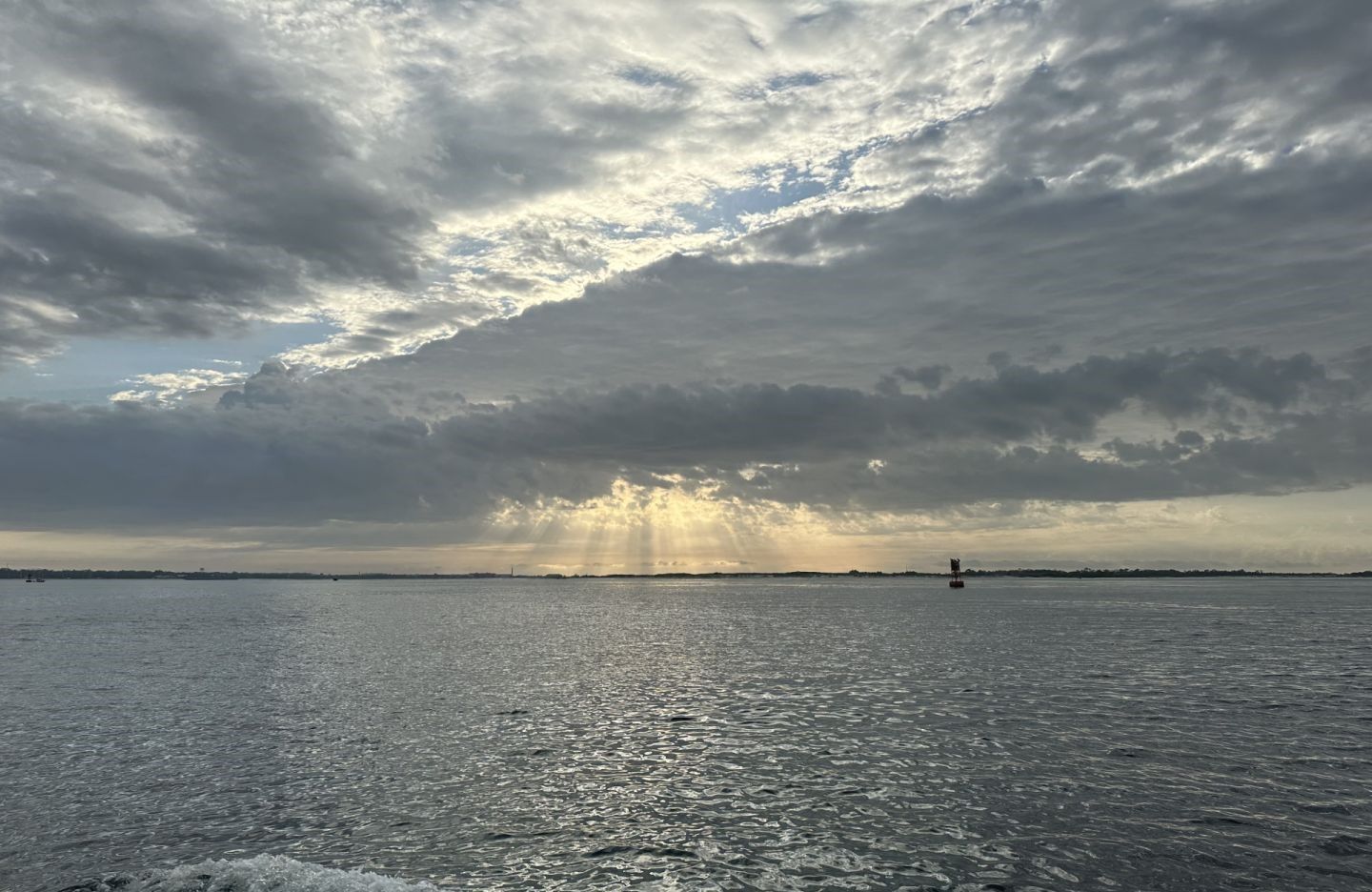 Dramatic cloudy sky with sunbeams breaking through over calm water with distant boat