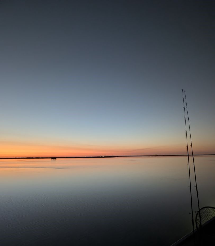 Fishing rods silhouetted against calm water during sunset with orange and blue sky reflection