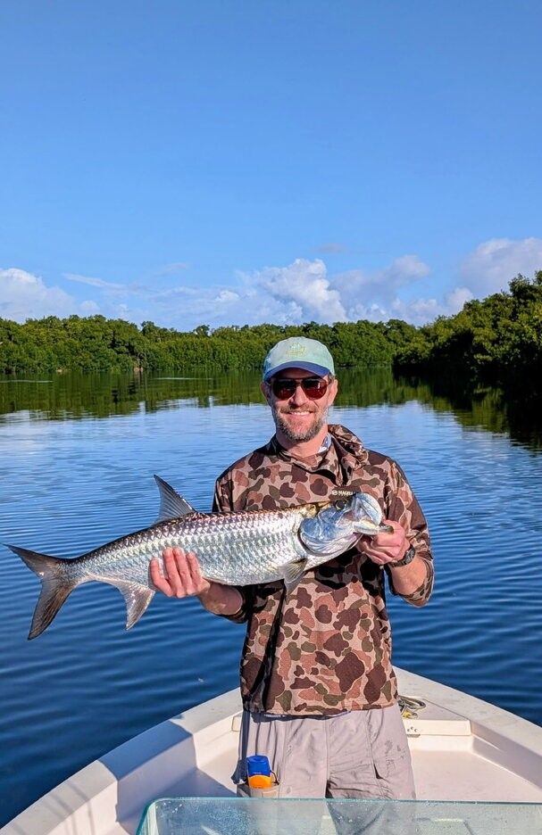 Angler holding caught tarpon on fishing boat in calm waters surrounded by mangroves