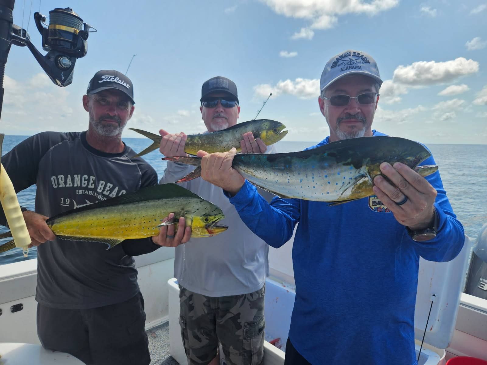 Three anglers displaying their caught mahi mahi fish on a fishing boat