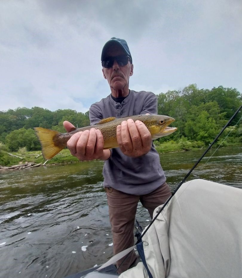 Freshly caught trout being held over river water with fishing rod visible