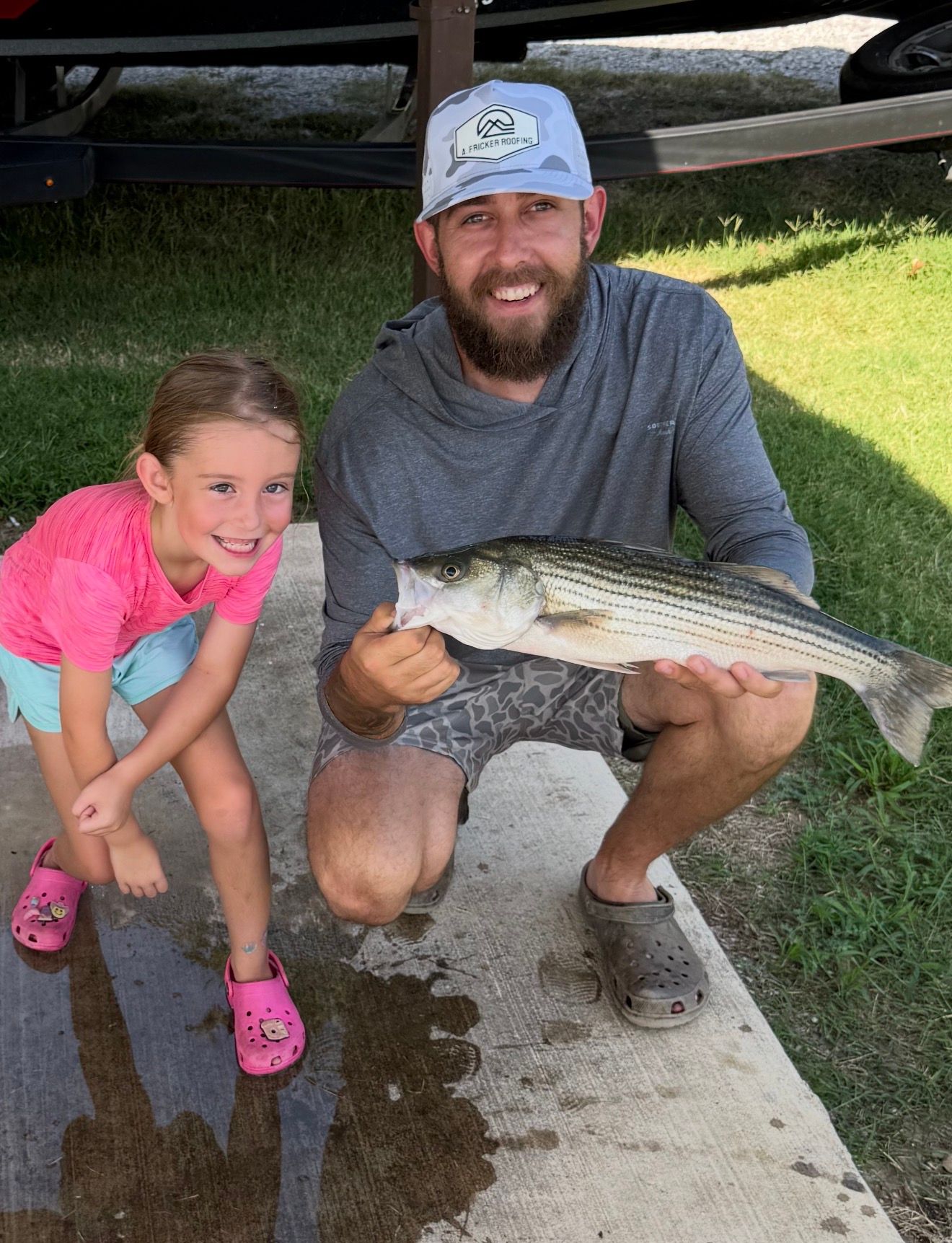 Striped bass catch displayed outdoors on concrete surface with boat trailer in background