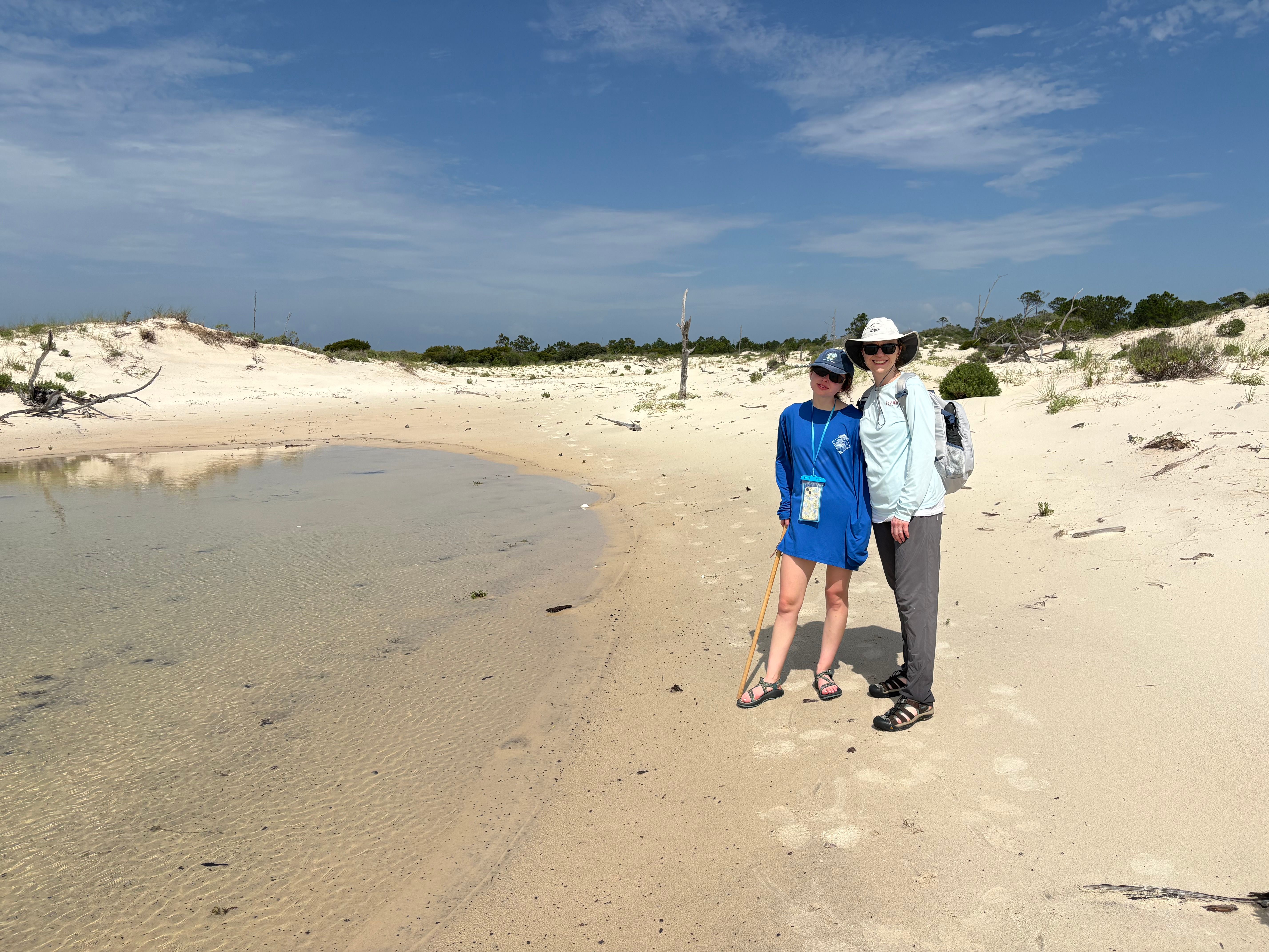Sandy beach with water pool and sand dunes under blue sky