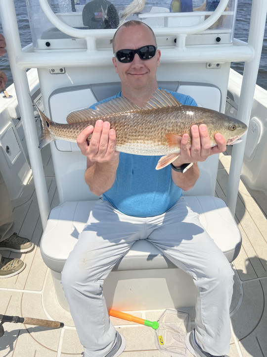 Reeling in a big redfish on a partly cloudy day with late afternoon rain.