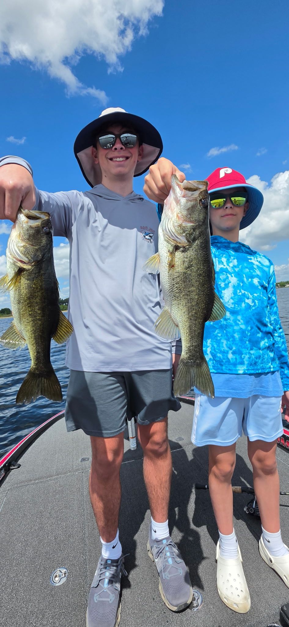 Two large bass fish being held up after a successful fishing trip on a lake