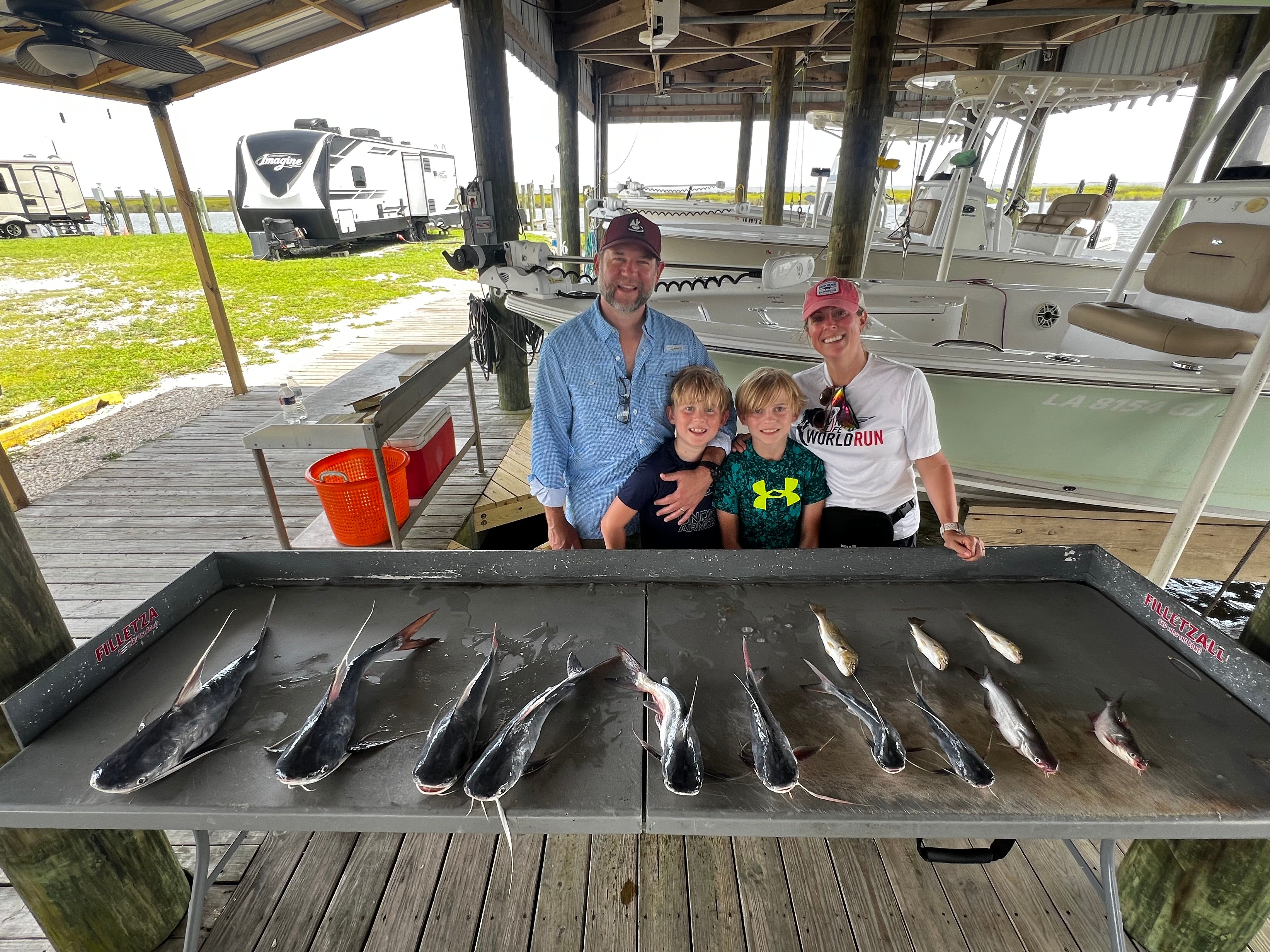Family fishing trip with successful catch of hardhead sea catfish displayed on cleaning table at marina dock