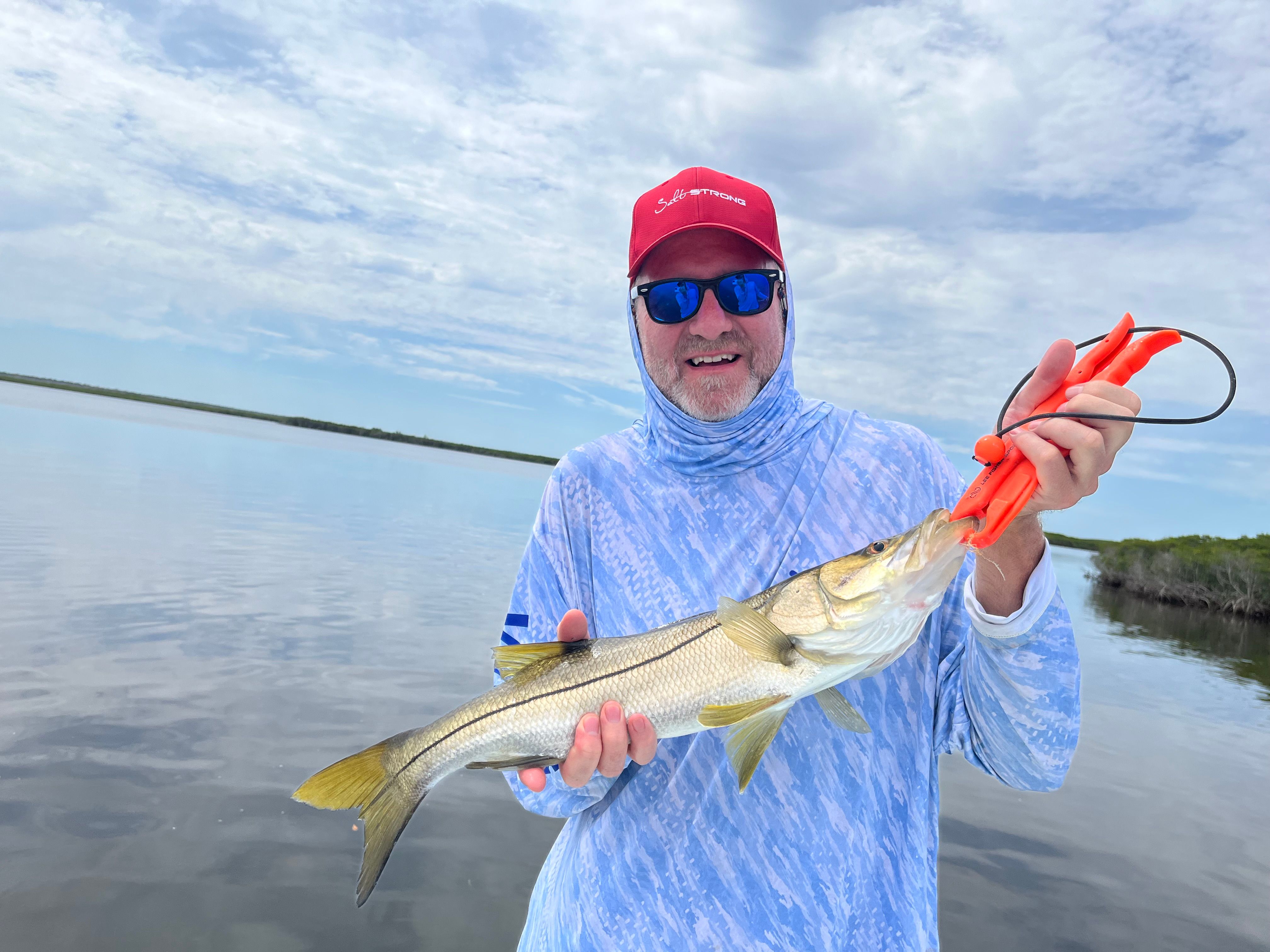 Angler holding freshly caught snook with fishing lure on boat in shallow water