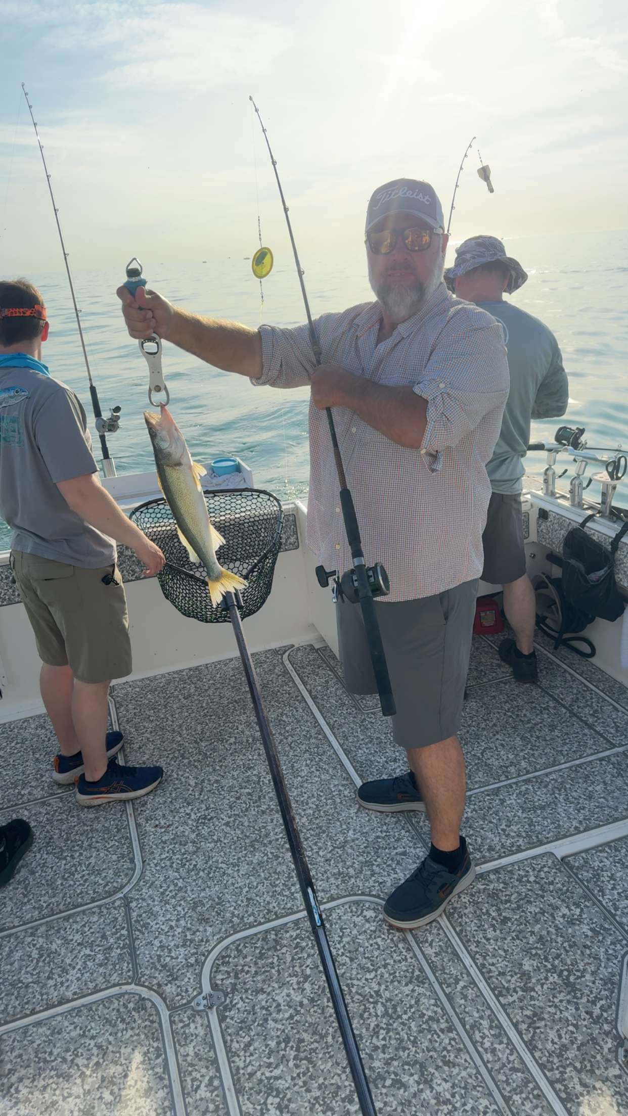 Freshly caught fish being held up on fishing boat deck with fishing rods and net visible