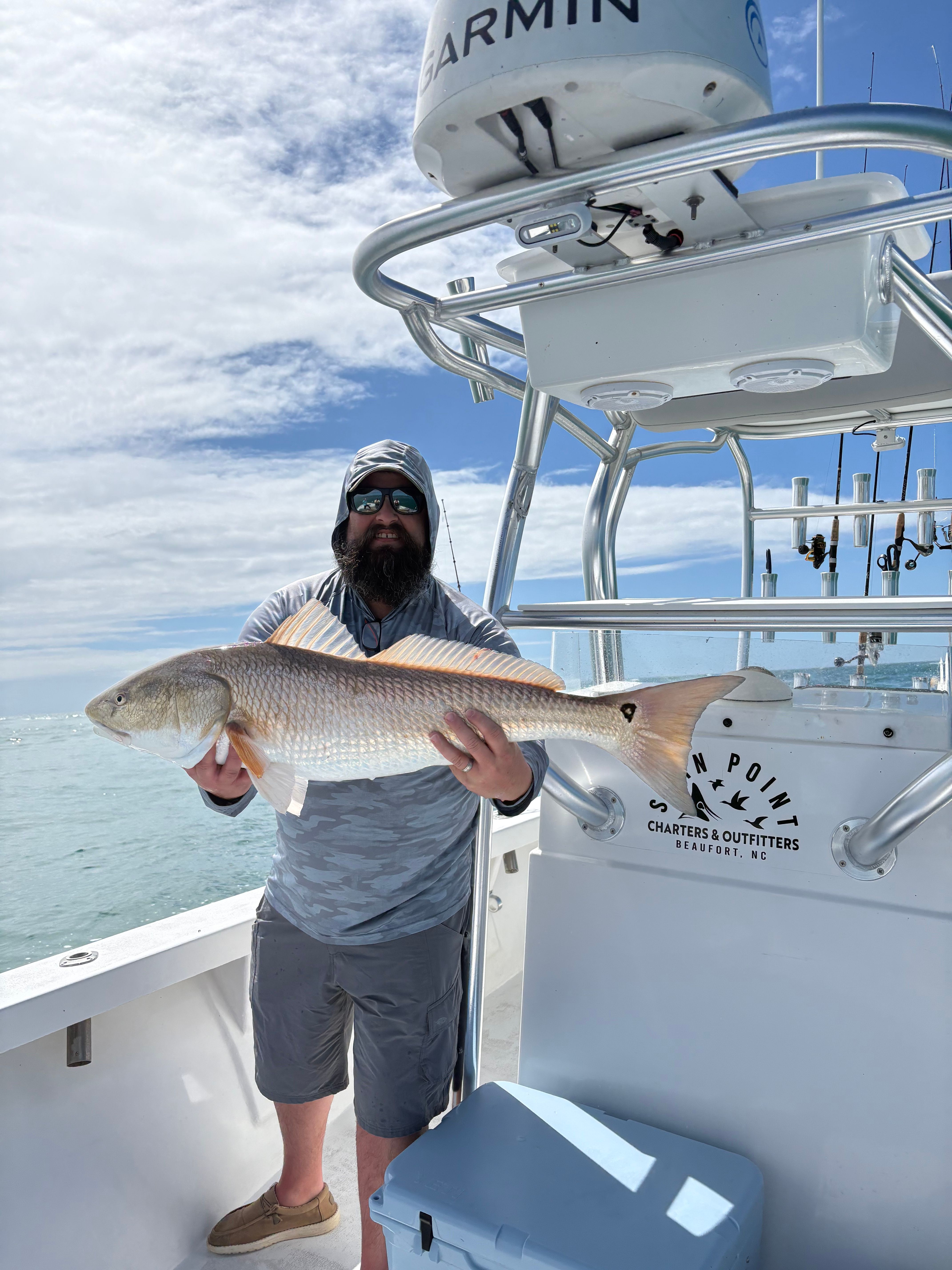 Large redfish caught on fishing boat deck with clear ocean waters and cloudy sky