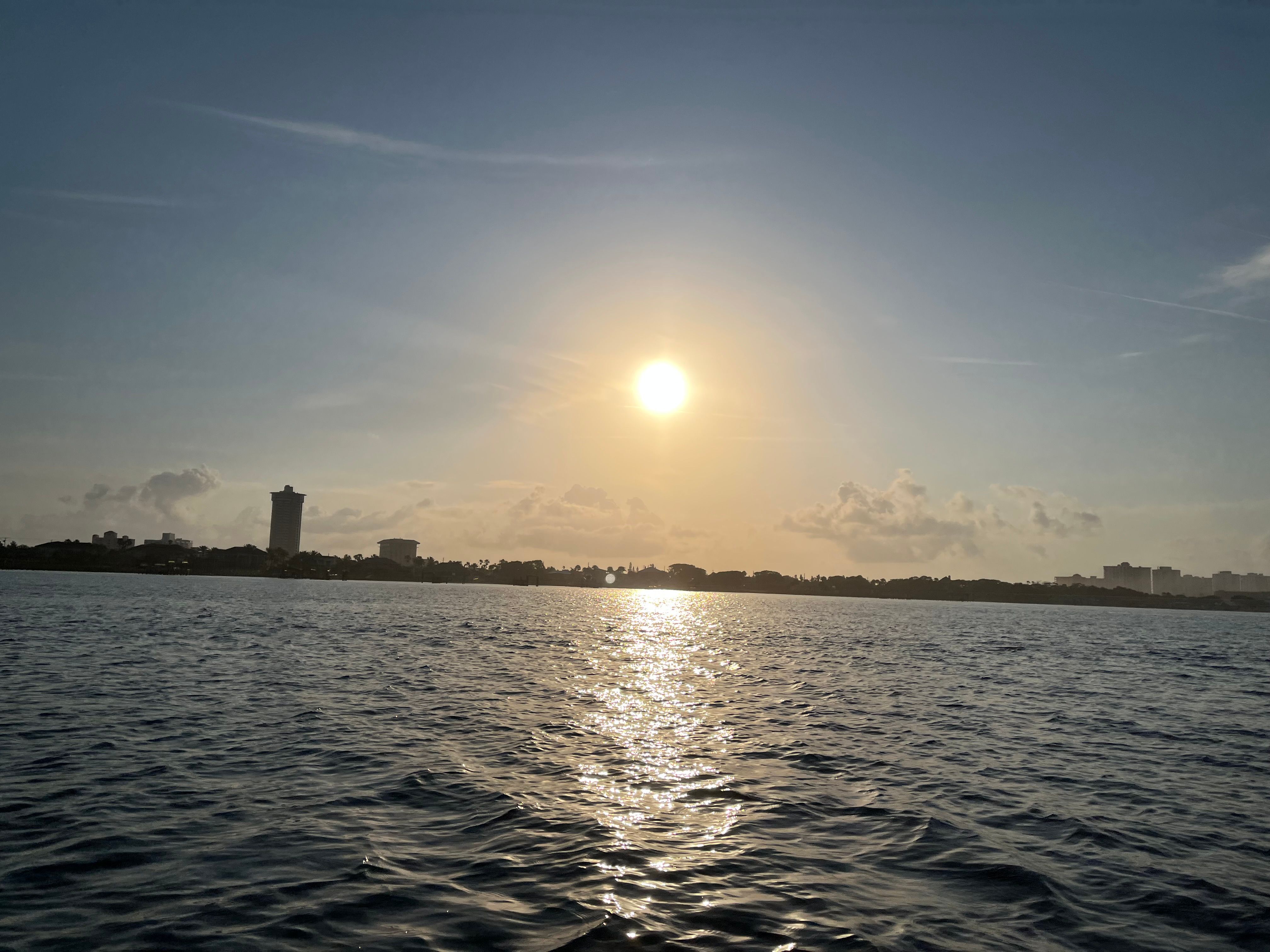 Sunset view over calm water with city skyline and buildings visible on the horizon