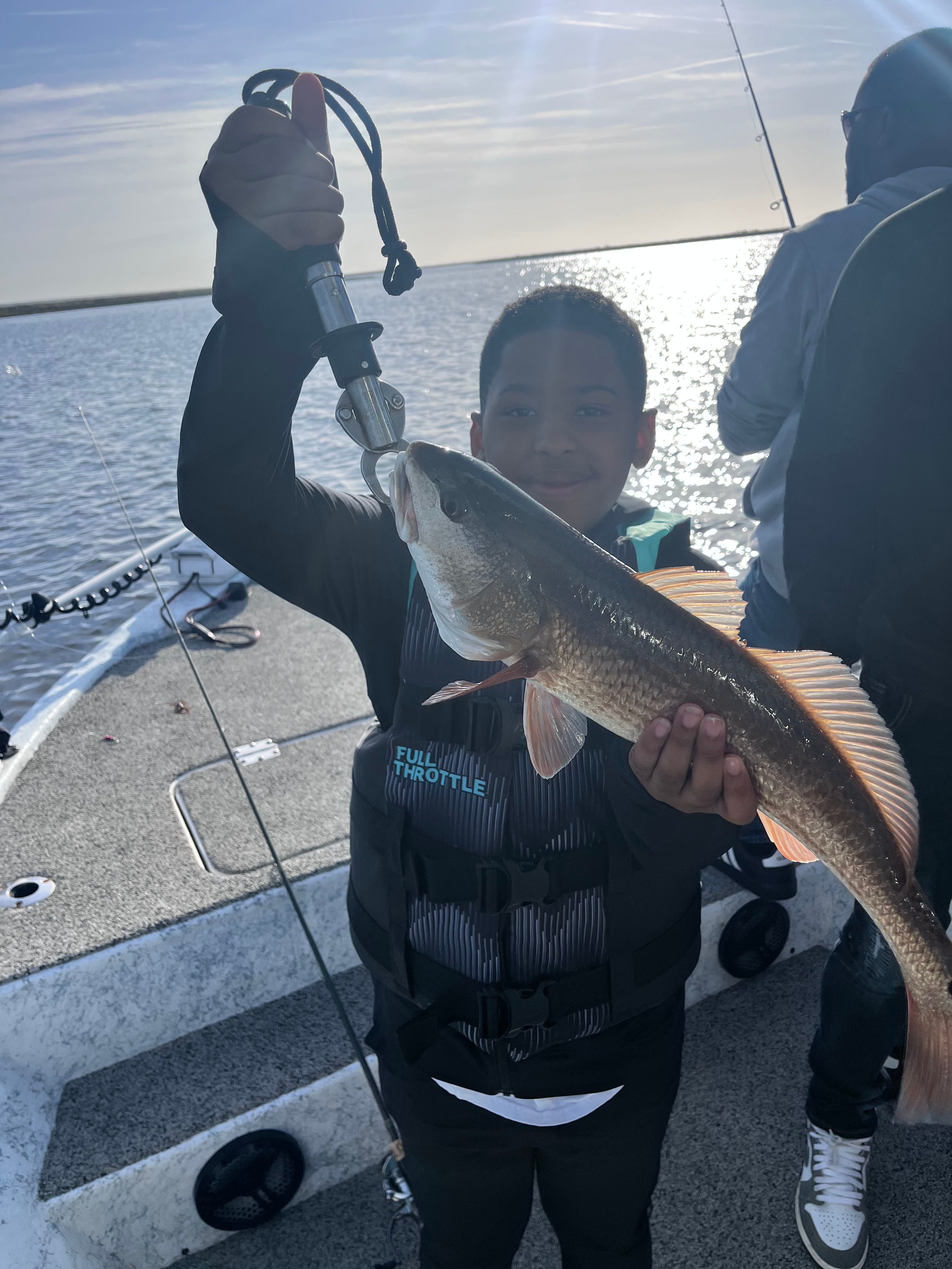 Angler holding a caught redfish on a boat deck during fishing trip