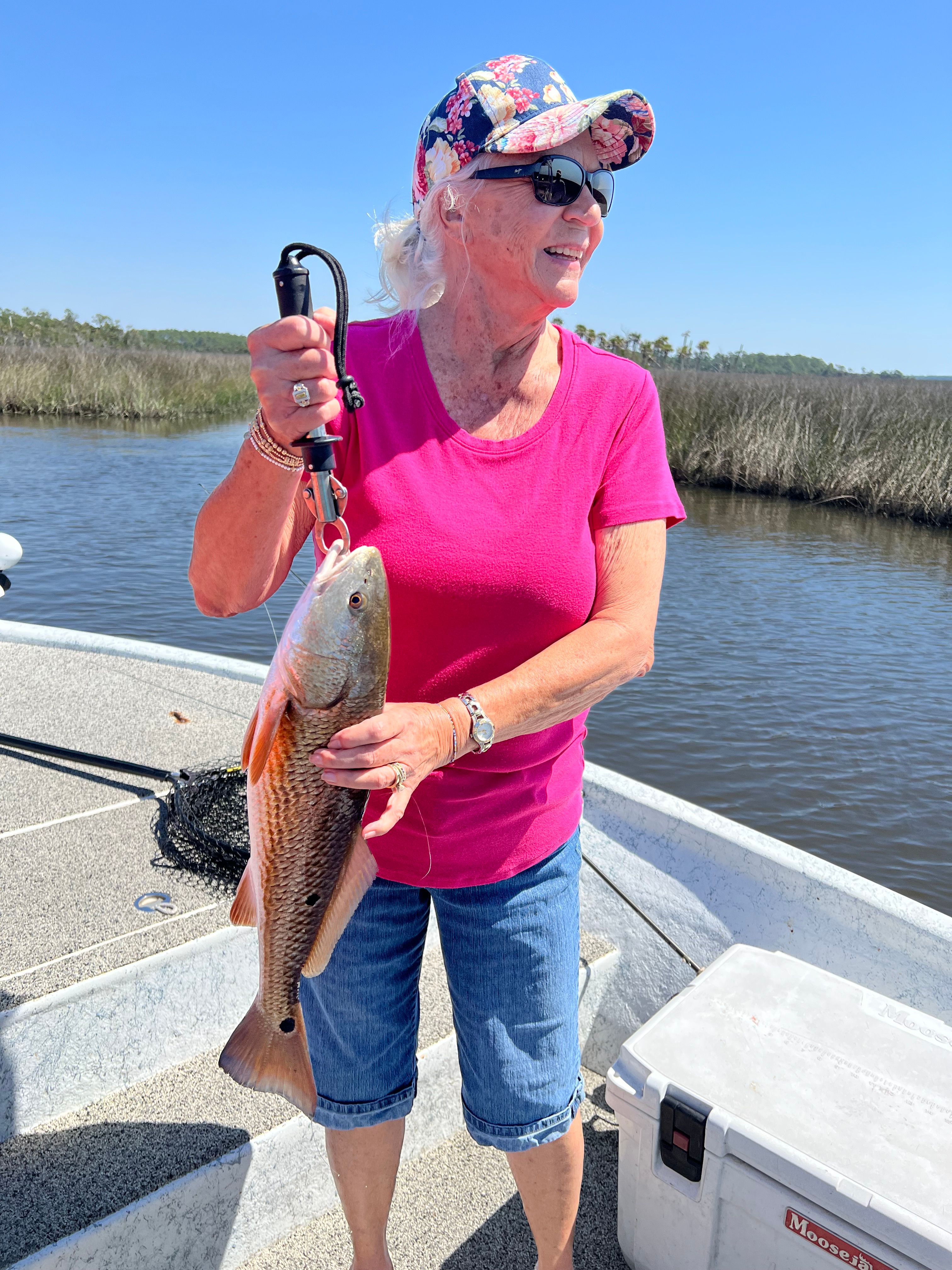 Angler holding freshly caught redfish on boat deck with water in background