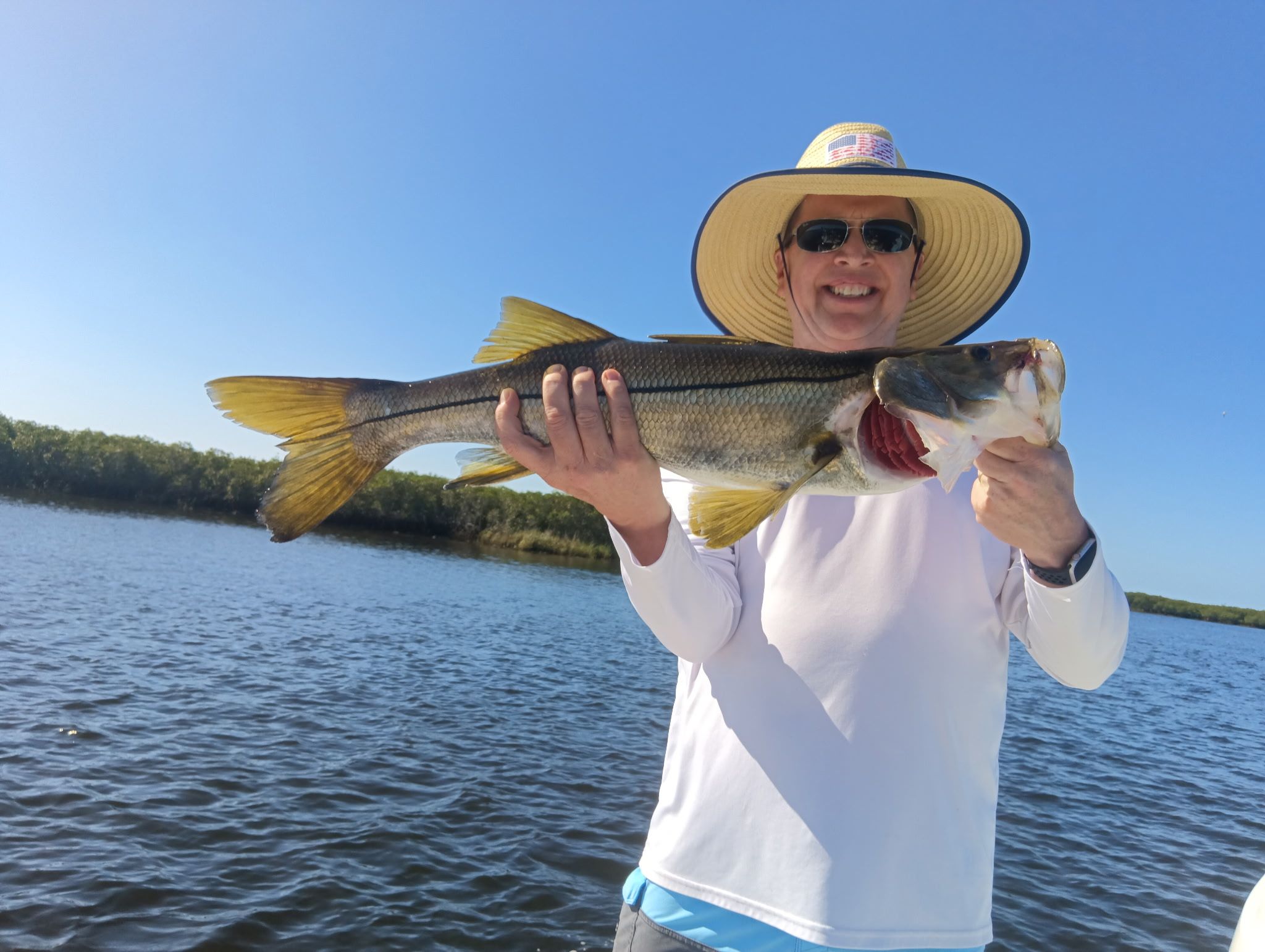 Angler holding large snook fish on boat with water and mangroves in background