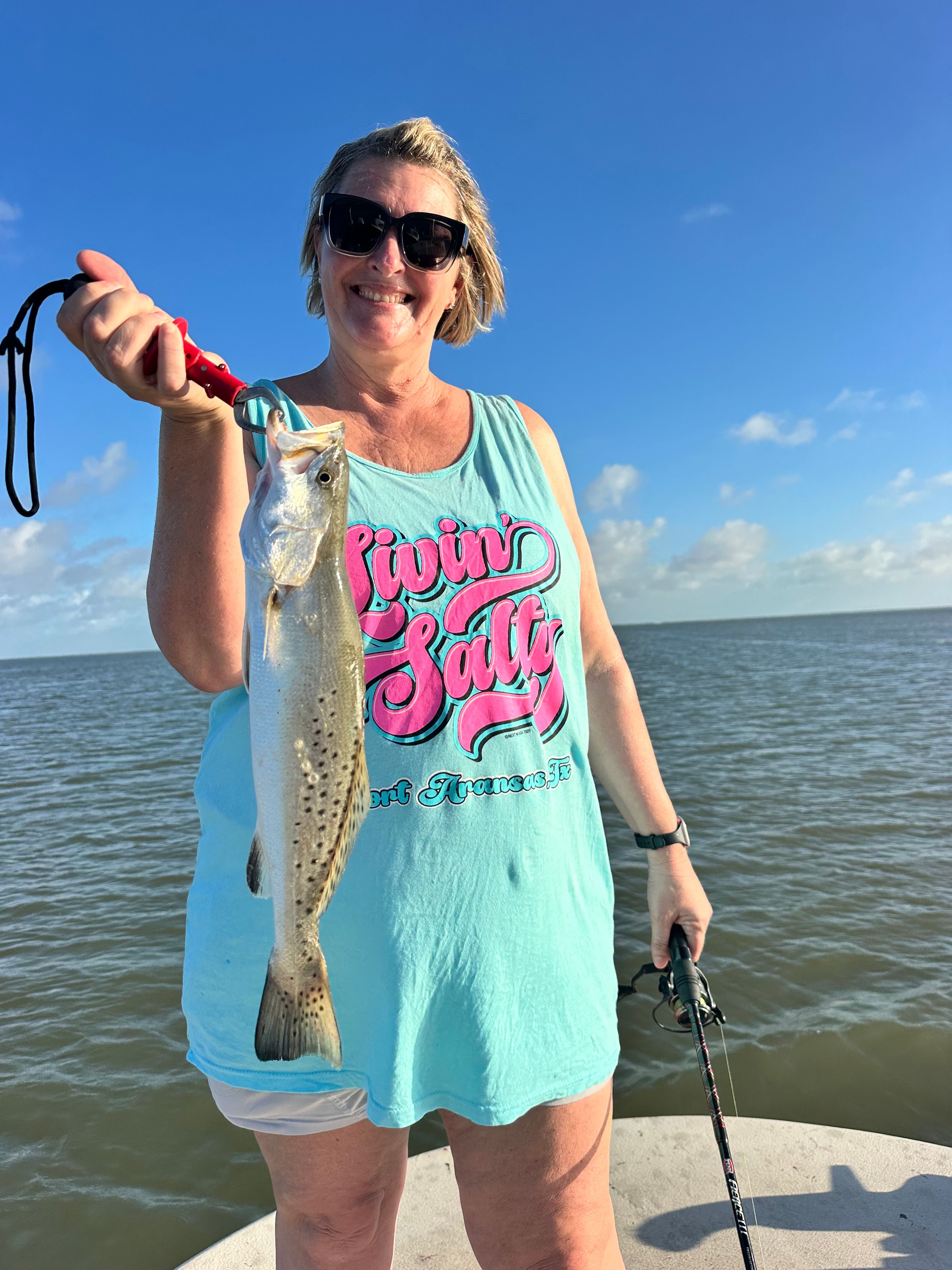 Angler holding freshly caught speckled trout with fishing rod on boat