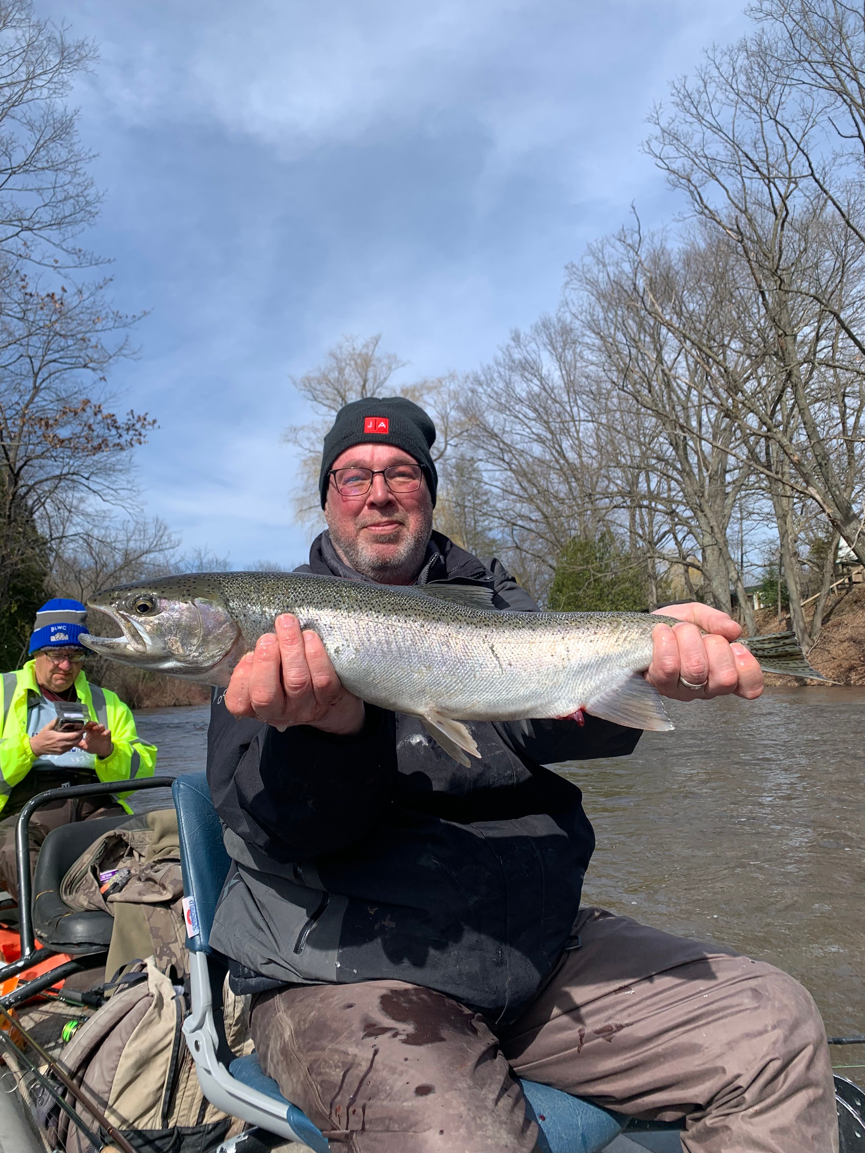 Angler holding a large rainbow trout catch outdoors by water