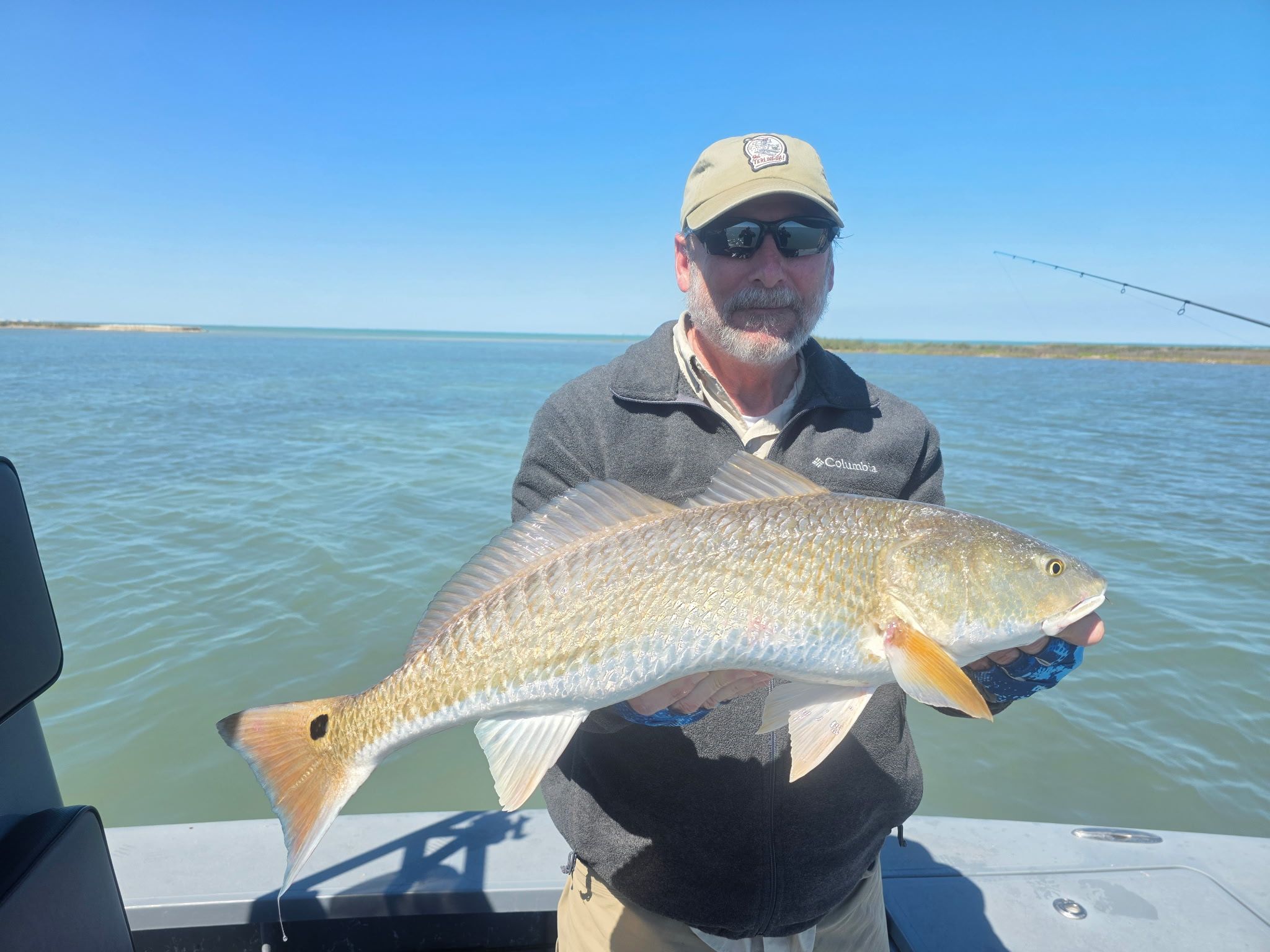 Angler holding large redfish on boat deck with blue water background