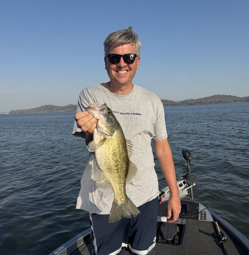 Angler holding freshly caught fish on boat with lake and hills in background