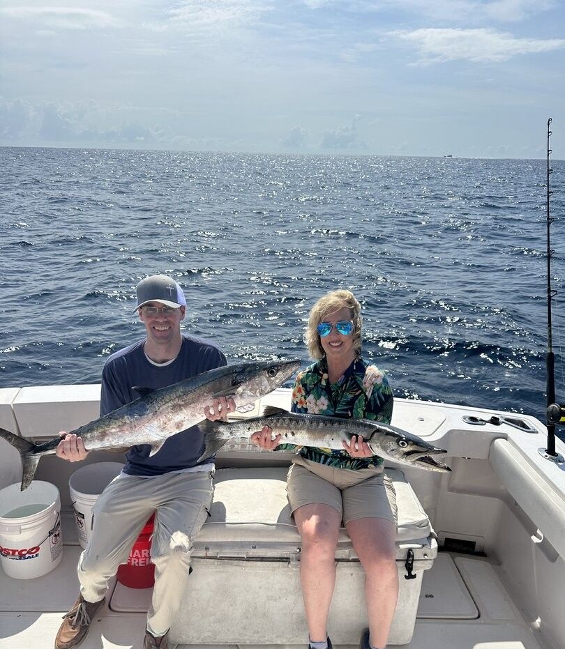 Two anglers on fishing boat displaying caught great barracuda and king mackerel on ocean