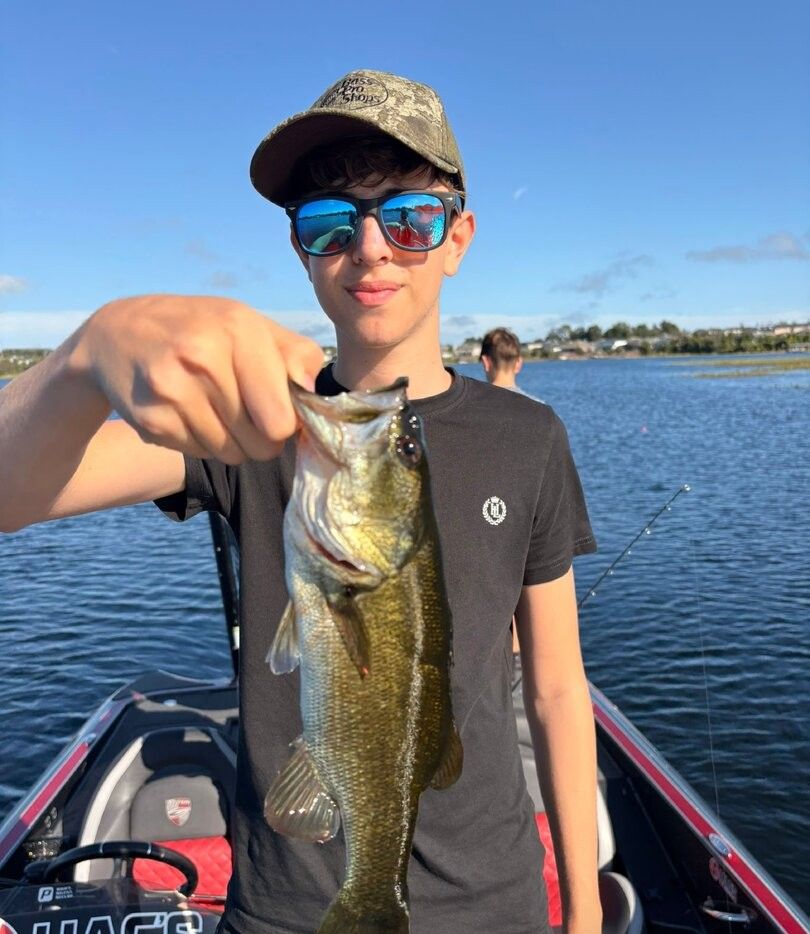 Fresh caught bass being held up on fishing boat with water and shoreline in background