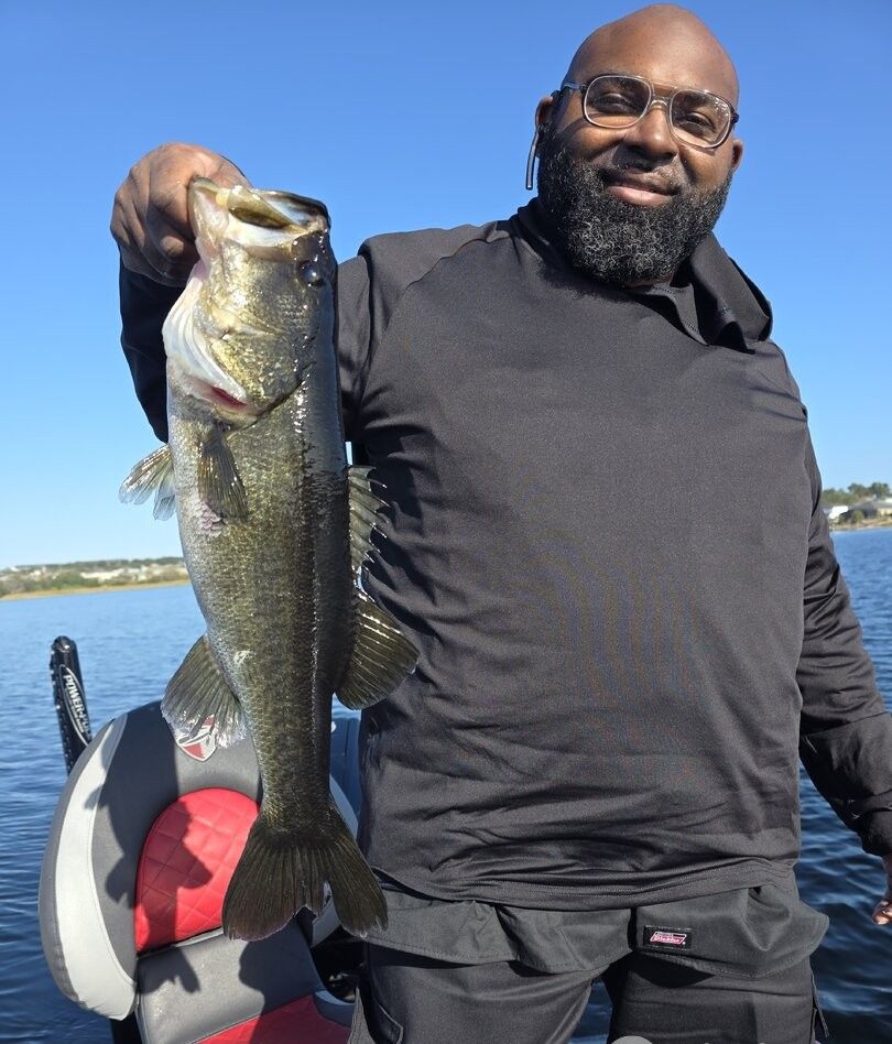 Large bass fish caught while fishing on lake with boat in background