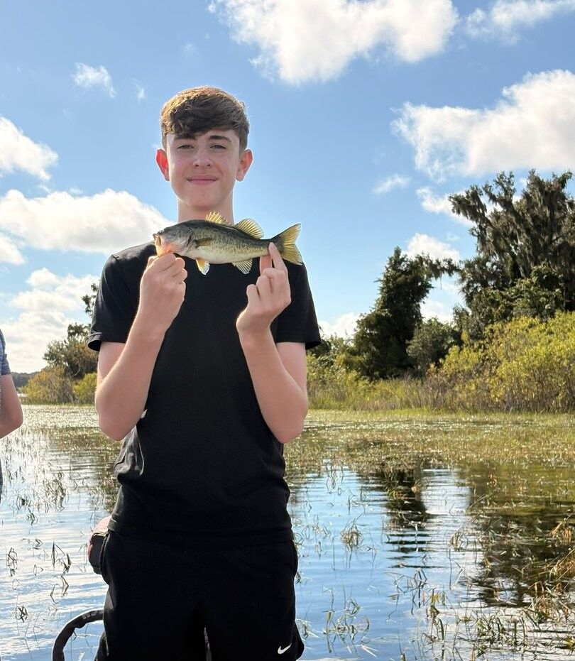 Angler holding freshly caught bass fish near shallow water with vegetation