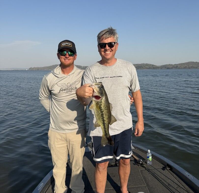 Two anglers on a boat displaying a freshly caught bass fish on the water